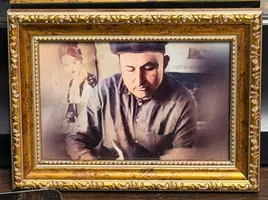 A hand-tinted vintage portrait of a barber in a cap, in a gilt frame